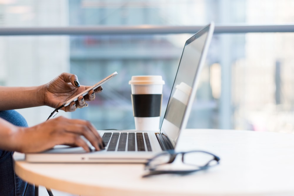 Person, die Smartphone und MacBook benutzt