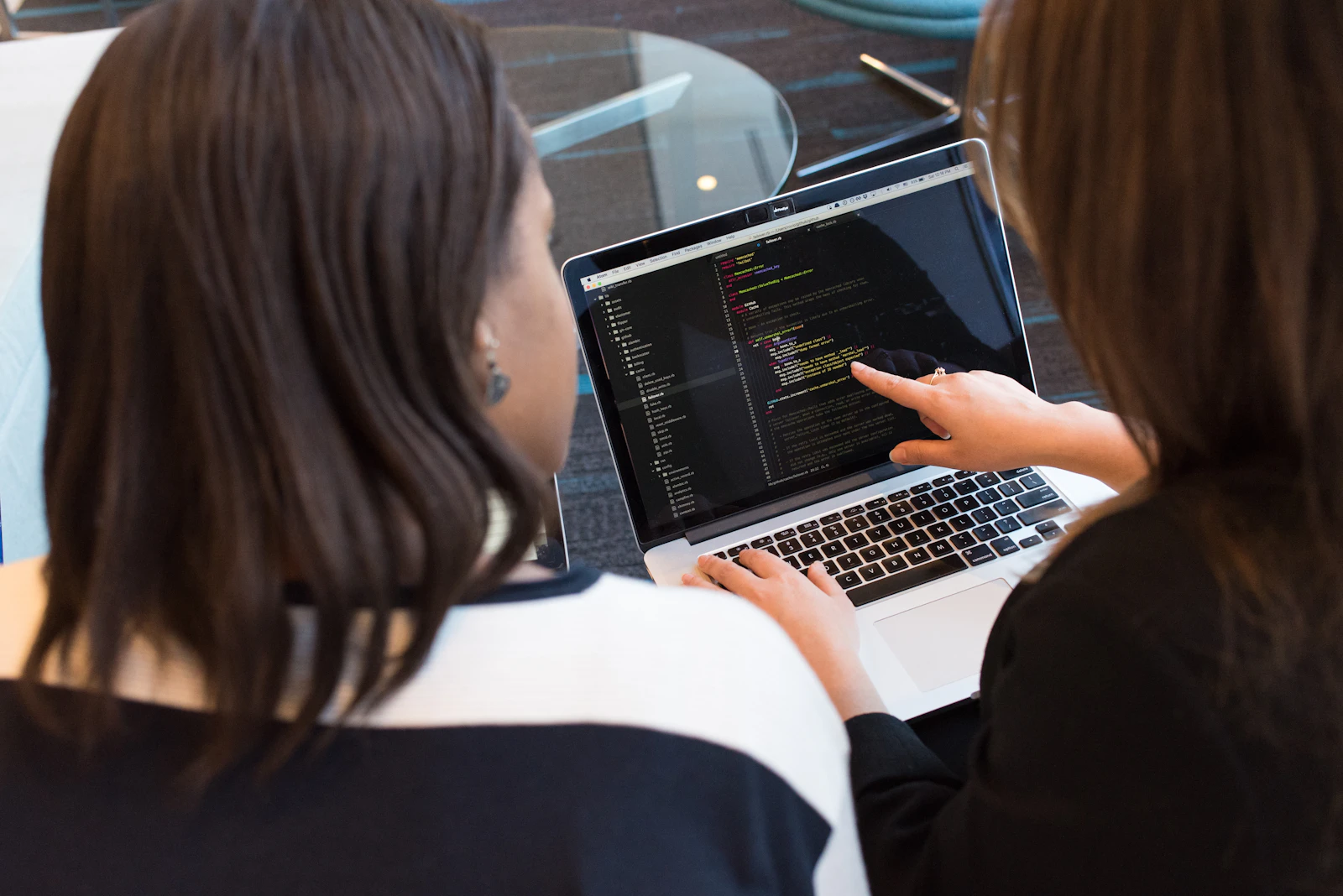 Two women collaborating and reviewing work together on a laptop in a tech workplace setting.