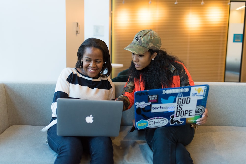 two women sitting on gray sofa with laptops