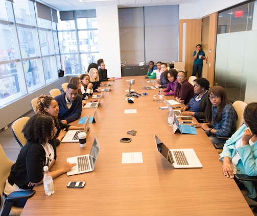 people sitting beside rectangular brown table with laptops