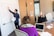 A group of people are in a meeting room. One person is standing and pointing at a whiteboard covered with diagrams and notes, while holding a piece of paper. Two other individuals are seated at a table with open laptops in front of them, appearing to be engaged in the presentation.