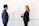 Two people engage in a discussion in front of a whiteboard filled with diagrams and flowcharts. One person is holding a red pen and a sheet of paper, while the other gestures with their hands, possibly explaining or elaborating on the ideas.