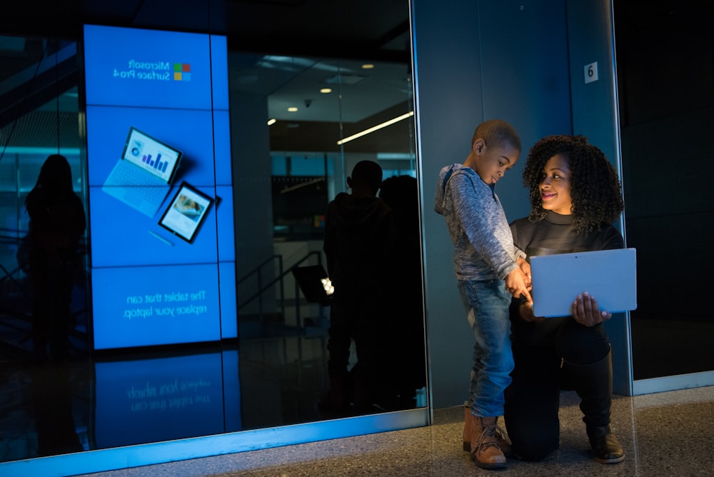 woman holding laptop beside toddler in gray jacket