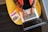A person is seated on a yellow chair, working on a laptop with visible code on the screen. Next to them, a book titled 'Python' is placed.