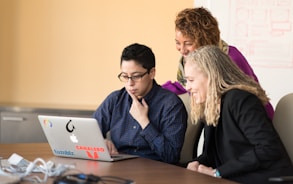 three women beside table looking at MacBook