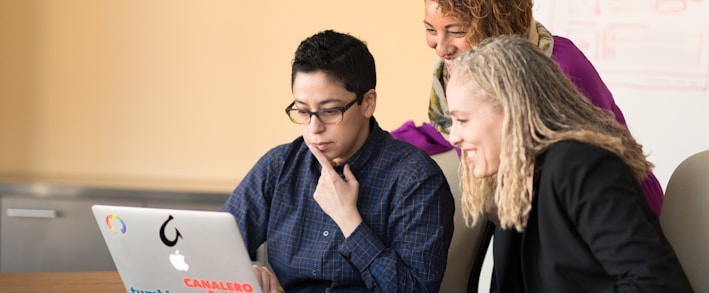 three women beside table looking at MacBook