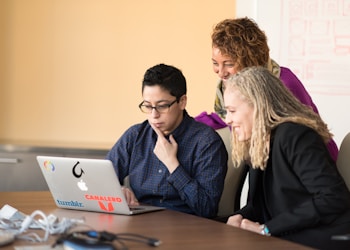 three women beside table looking at MacBook