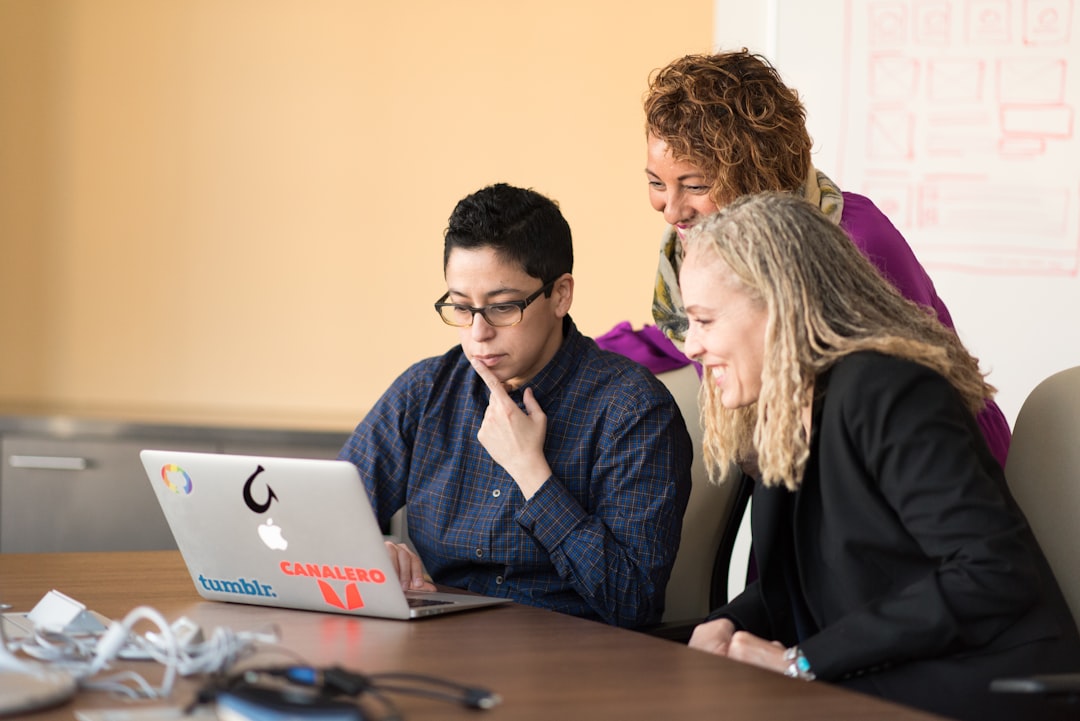 three women beside table looking at MacBook,