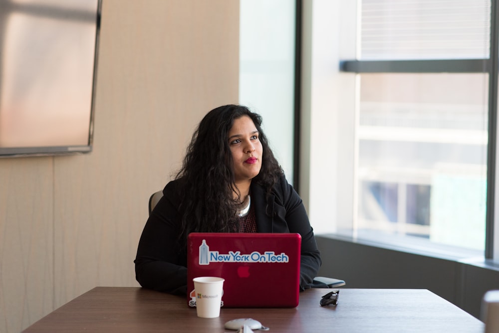 woman in black long-sleeved shirt using laptop beside glass window