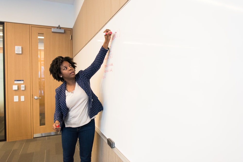 a woman writing on a whiteboard in a hallway