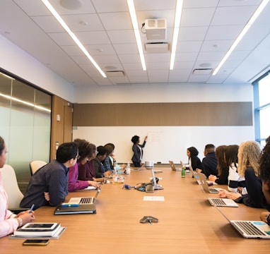 people on conference table looking at talking woman