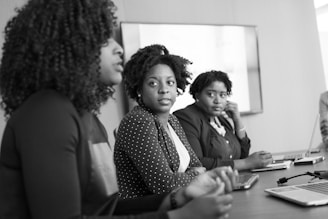 grayscale photography of two women on conference table looking at talking woman