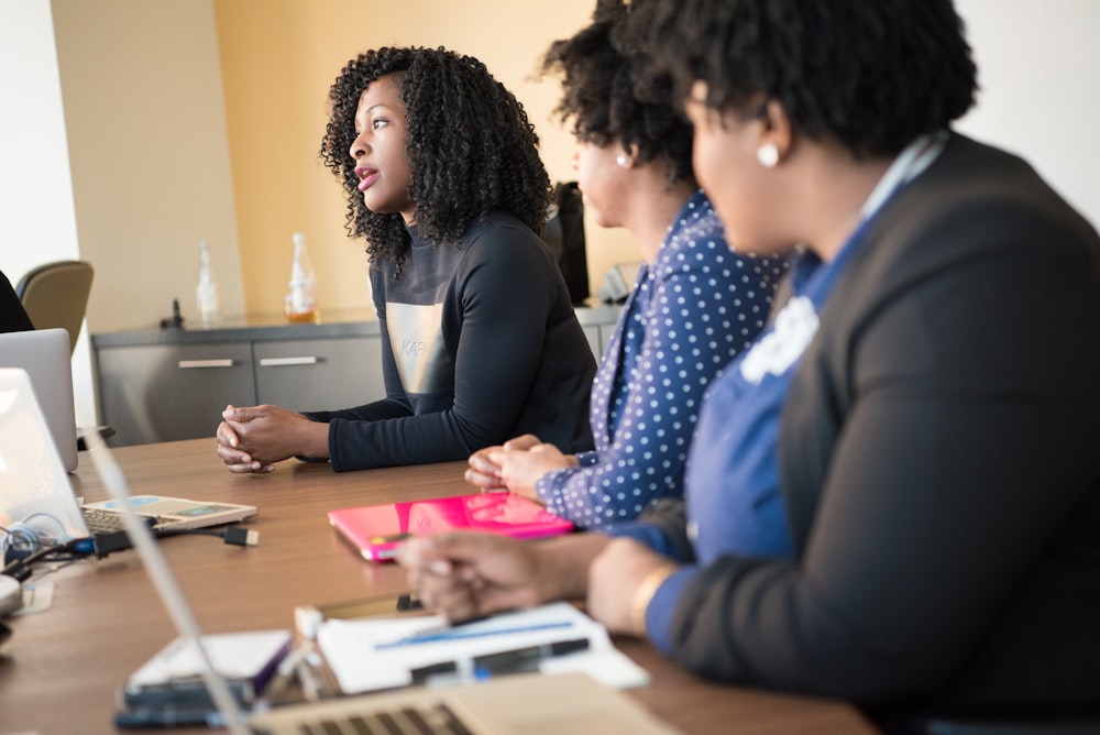 two women sitting at table looking at talking woman