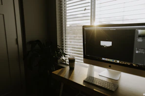 A serene workspace with a laptop, coffee cup, and gold-accented notebook beside a window with sunlight streaming in.