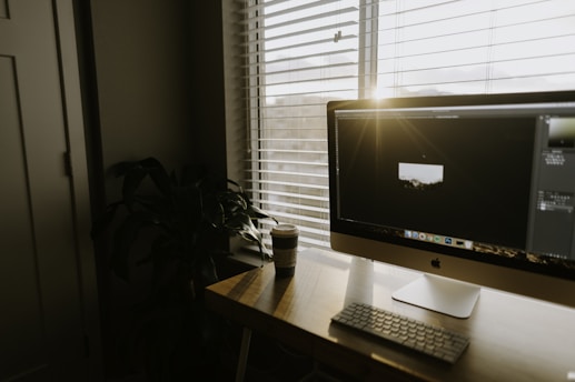 A cozy workspace with a laptop, a cup of coffee, and a small plant on a wooden desk bathed in morning light.