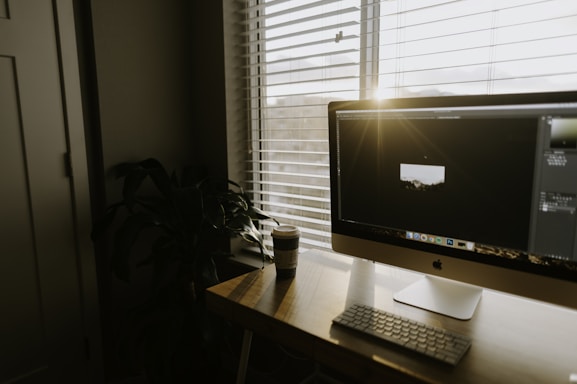 A cozy workspace with a laptop, coffee cup, and a small plant beside a window letting in warm sunlight.