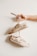 A hand holding a pair of beige sneakers that are creatively personalized with floral designs and the phrase 'bloom where you are planted'. The sneakers hang on a beige background, giving a minimalist and artistic vibe.