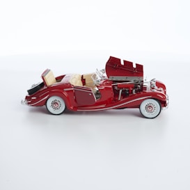 A detailed model of a vintage red convertible car with an open hood and intricate detailing. The car has whitewall tires and chrome accents, showcasing the engine and luxurious interior with beige seats.