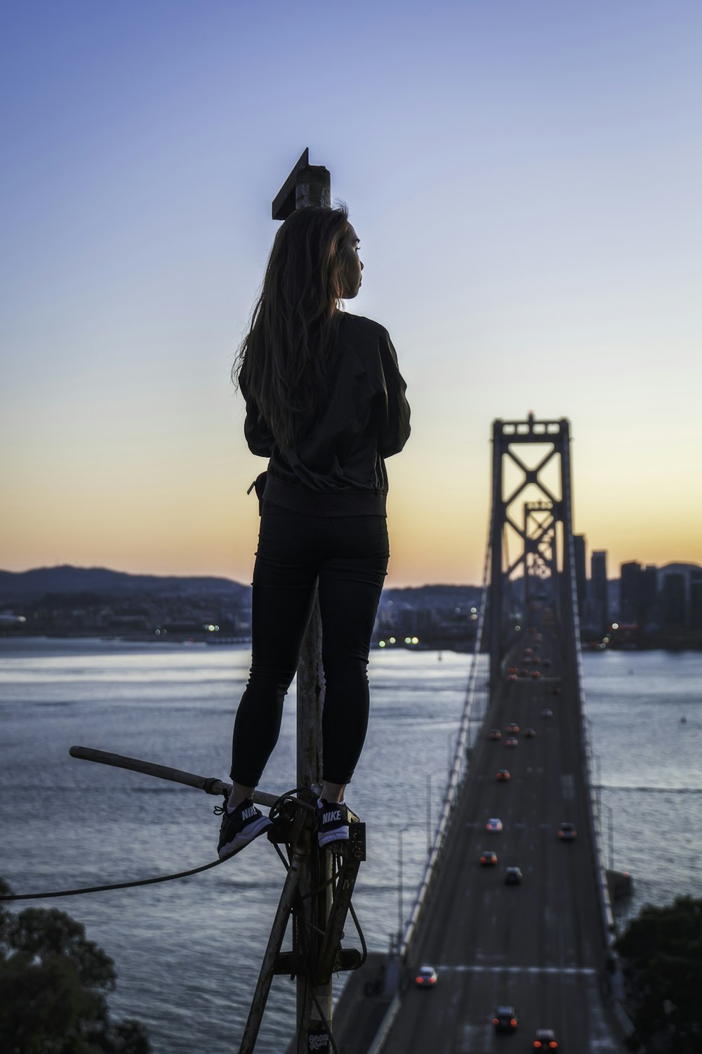 woman standing on metal pole looking at Oakland Bay Bridge during golden hour