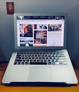A laptop with an open screen displaying multiple photos, placed on a wooden surface. To the left is a small religious image stuck on the wall.