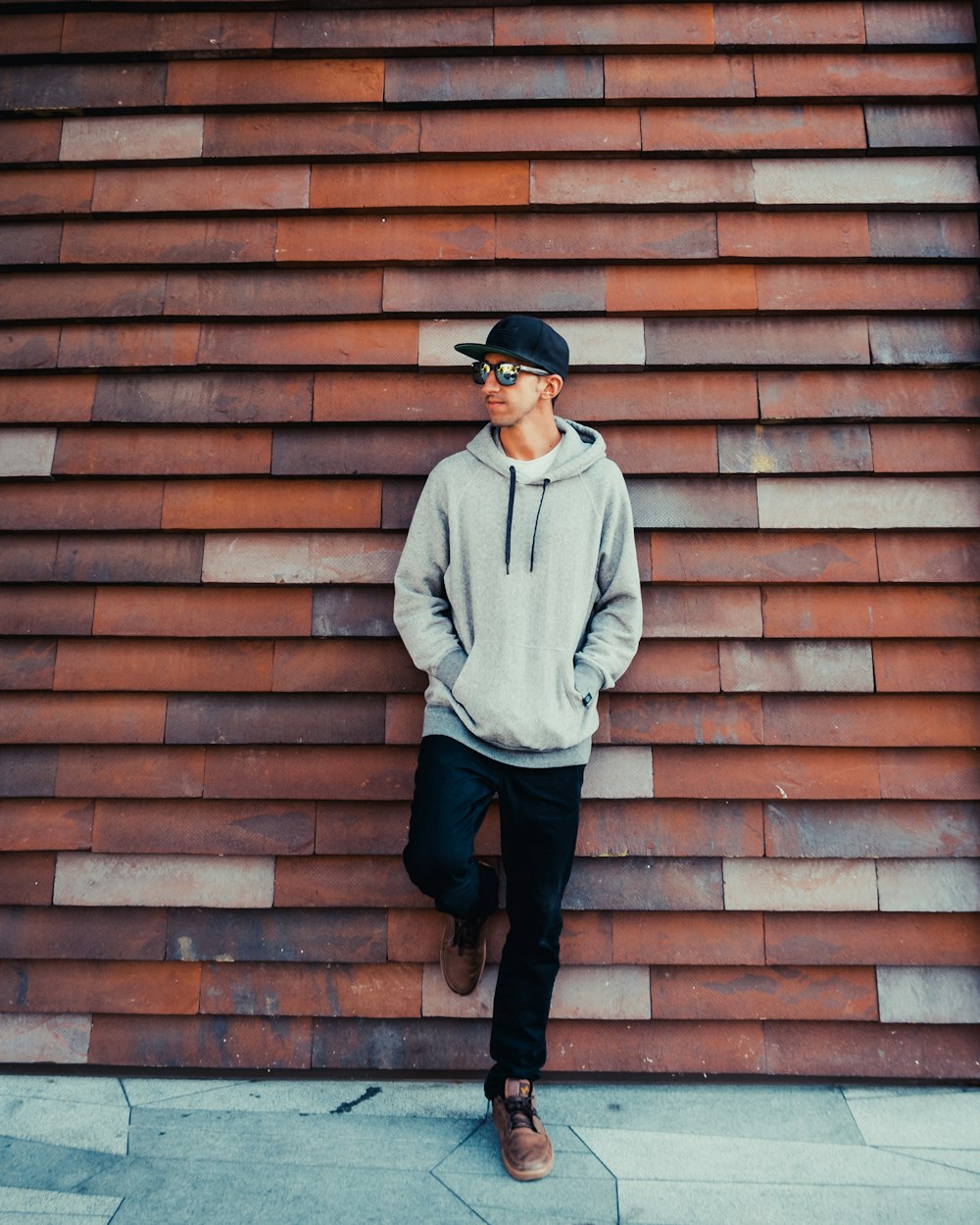 man wearing pullover hoodie and sunglasses leaning on wall