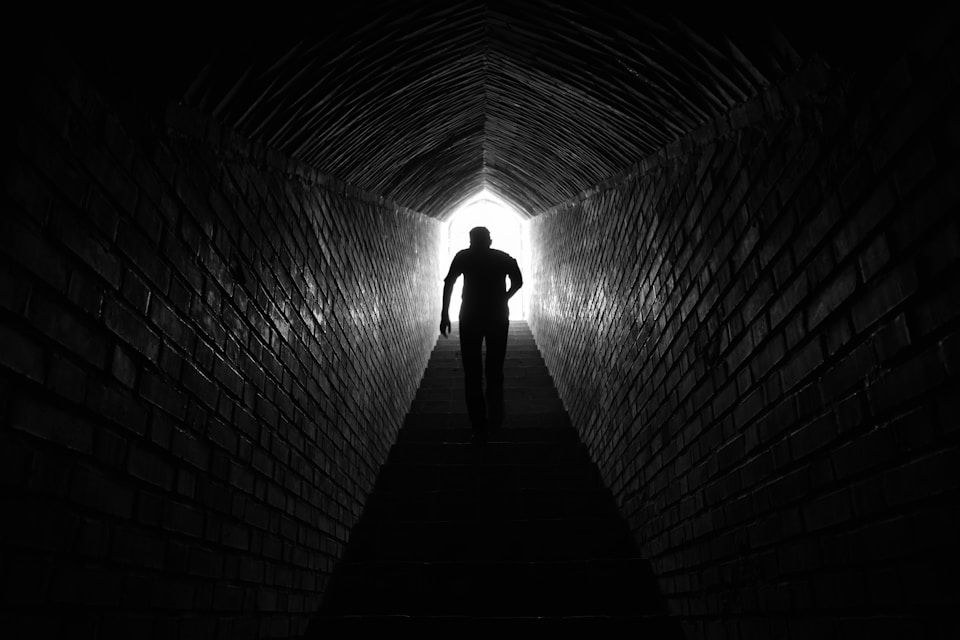 Silhouette of a person climbing stairs toward the light at the end of a tunnel