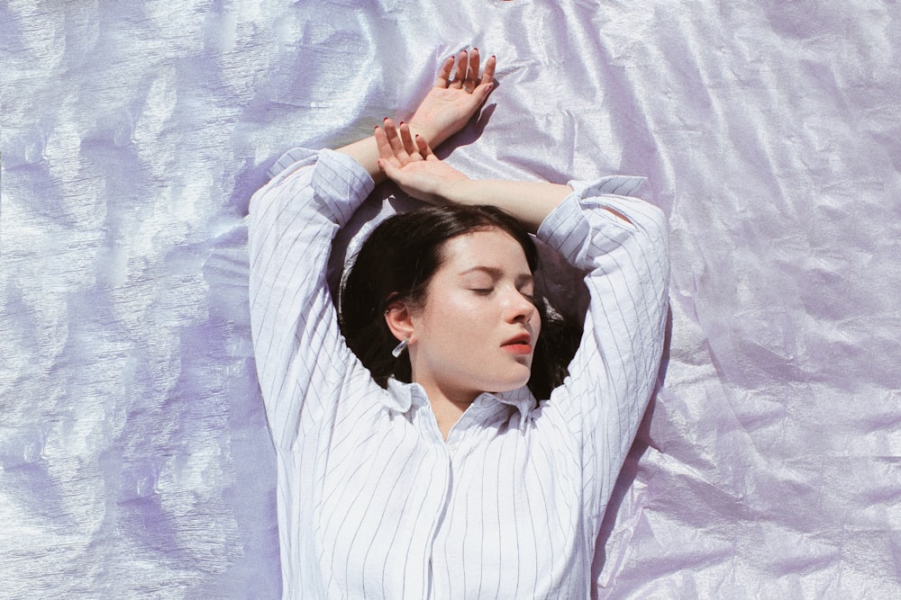 woman in gray and white pinstriped shirt lying on gray sheet