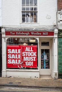 Sale Sale Sale and All Stock Must Go! signs on The Edinburgh Woollen Mill building windows during daytime