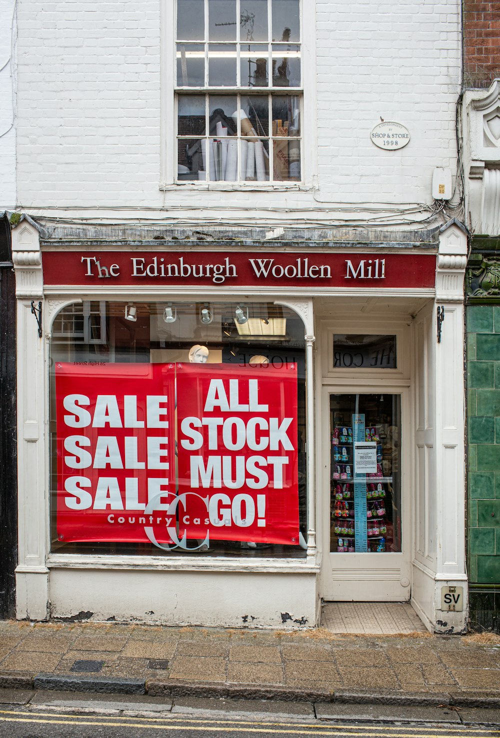 Sale Sale Sale and All Stock Must Go! signs on The Edinburgh Woollen Mill building windows during daytime
