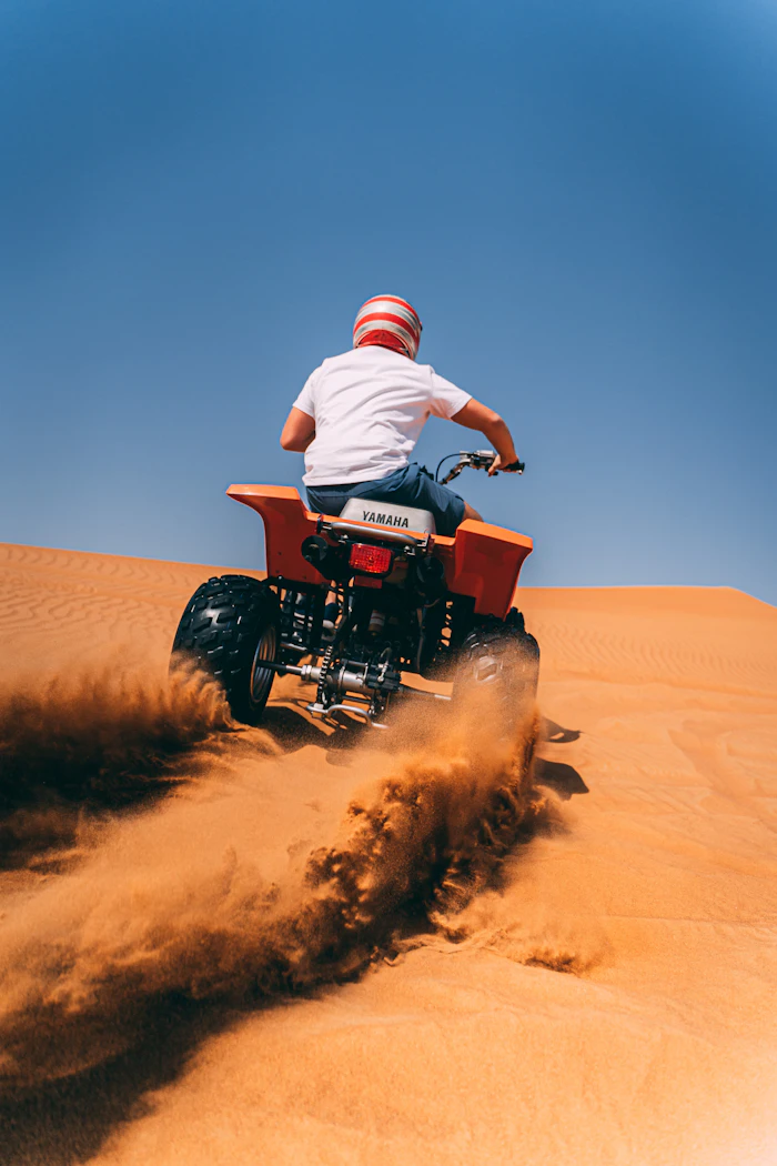Person riding a quad bike (ATV) across desert sand dunes