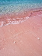 A sunlit beach with turquoise waves curling gently onto pink sand.