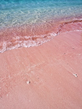 A sunlit beach with turquoise waves curling gently onto pink sand.