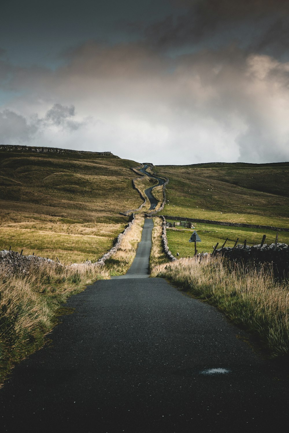 road between green grasses under cloudy sky during daytime