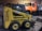 A yellow skid steer loader with the label 'GEHL 4625 SX' is parked inside a garage or workshop. There's an orange dump truck with the name 'Weston' visible in the background.