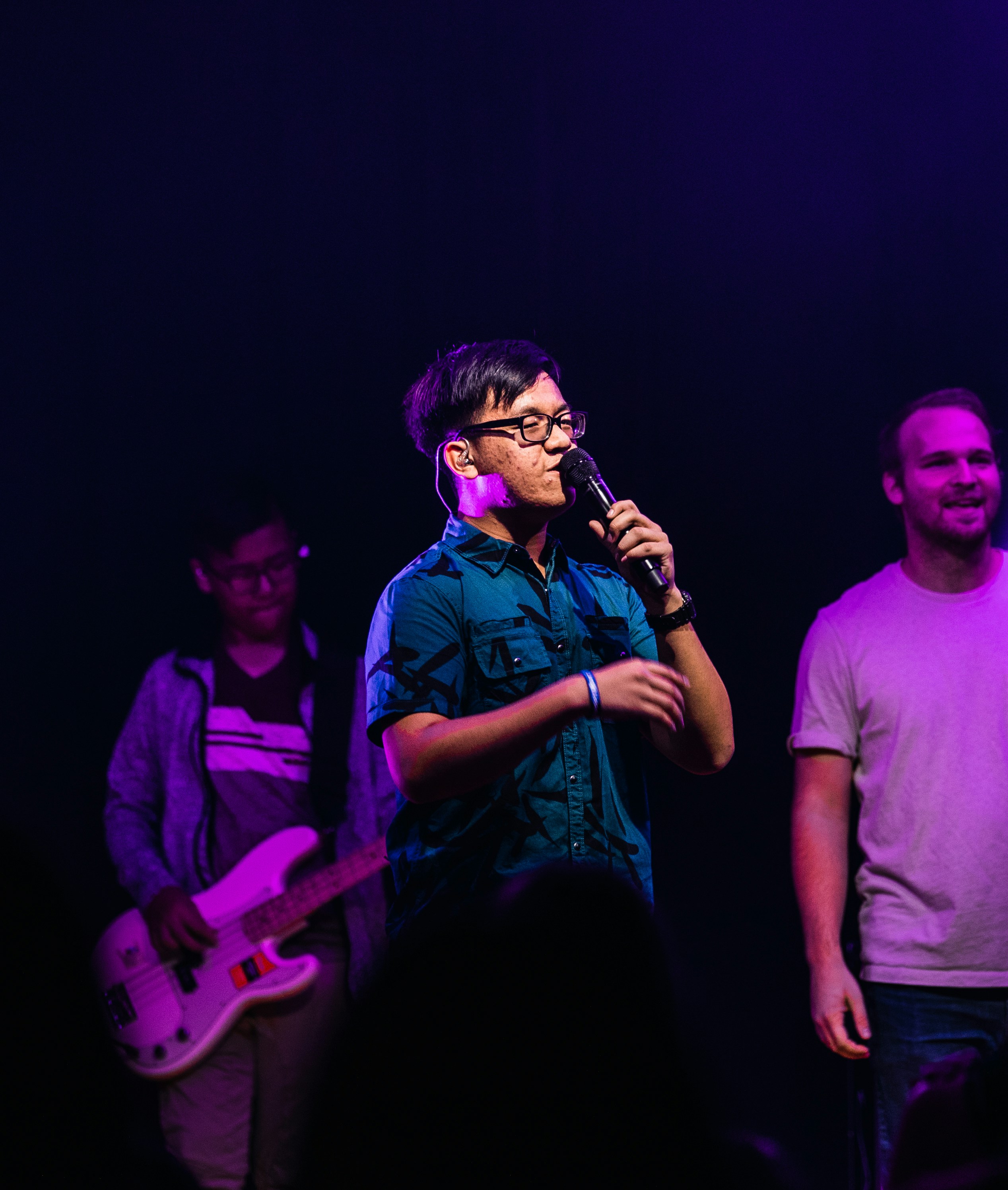 A Singer, Singing on  a stage with a couple people behind him in the foreground