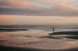A serene beach at sunset with a lone traveler walking along the shore.