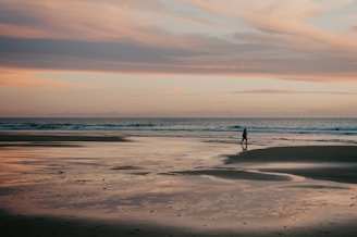 A serene beach sunset with a lone traveler reflecting by the shore.