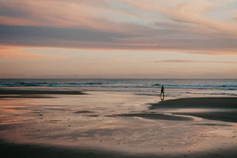 A solo traveler relaxing on a serene beach at sunset, waves gently lapping nearby.