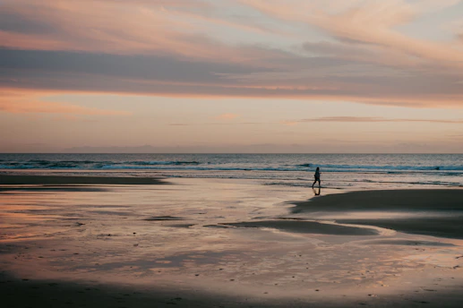 A vibrant sunset over a peaceful beach with a lone traveler walking along the shore.