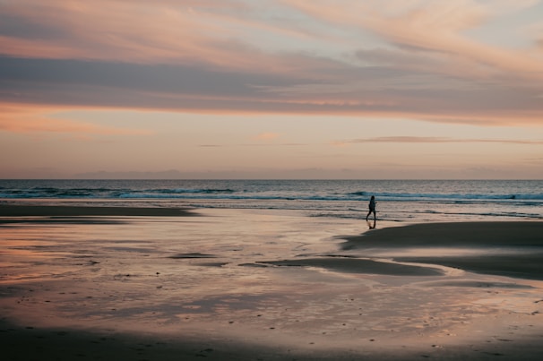 Sunset over a serene beach with gentle waves and a lone traveler walking
