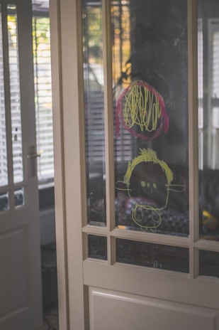 A cheerful child proudly showing a drawing to their parent in a sunny kitchen.