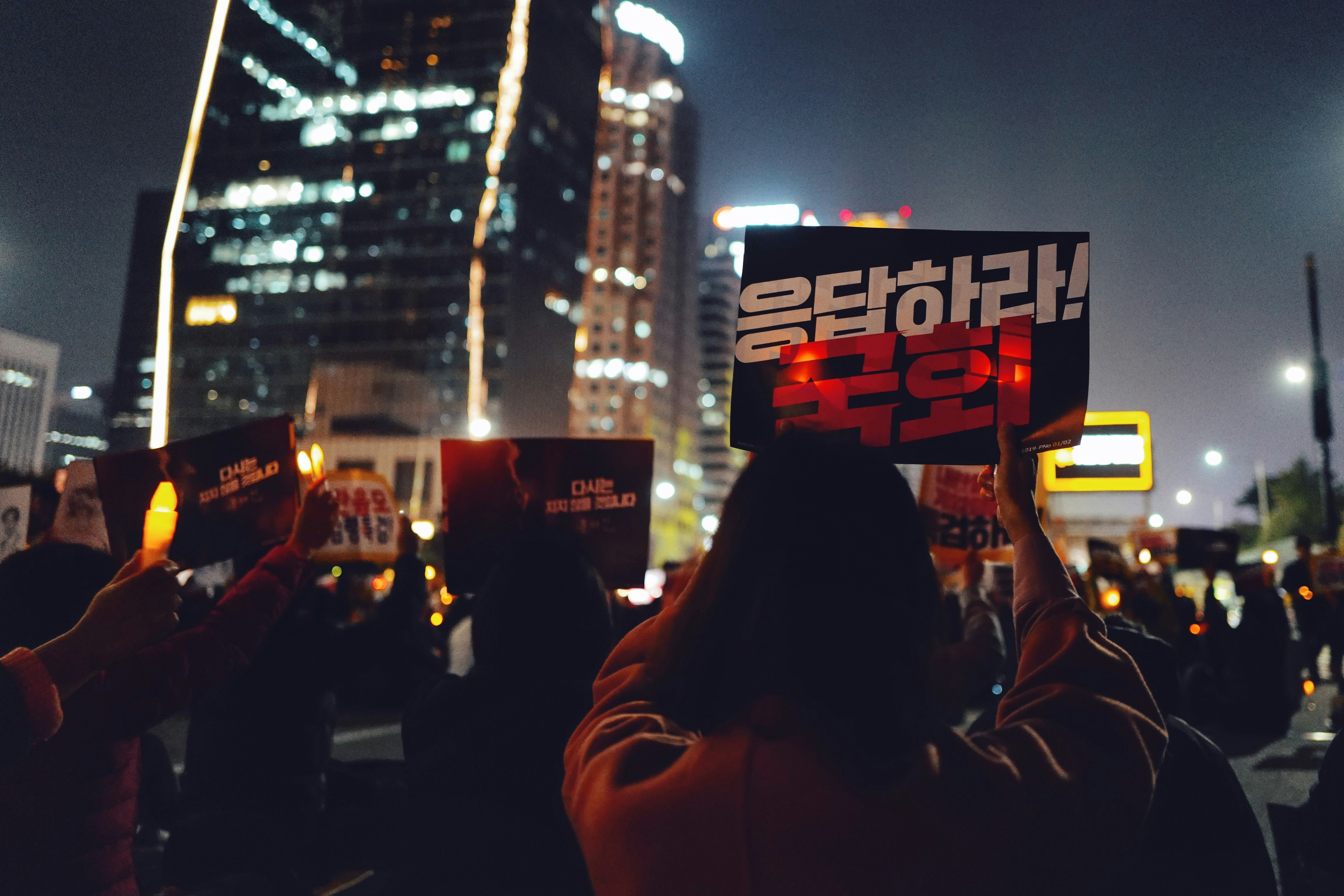 selective focus photography of crowd holding Hangul signs at night