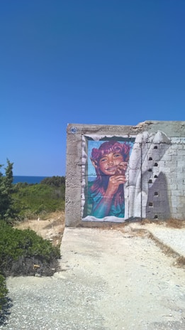 A preteen smiling while painting a bright mural on a wall outdoors.