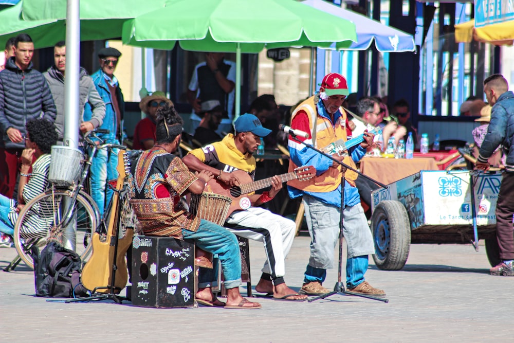 three person playing musical instrument beside green tent during daytime