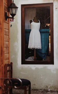 Warm off-white artisanal dress displayed on a mannequin against a natural linen backdrop.