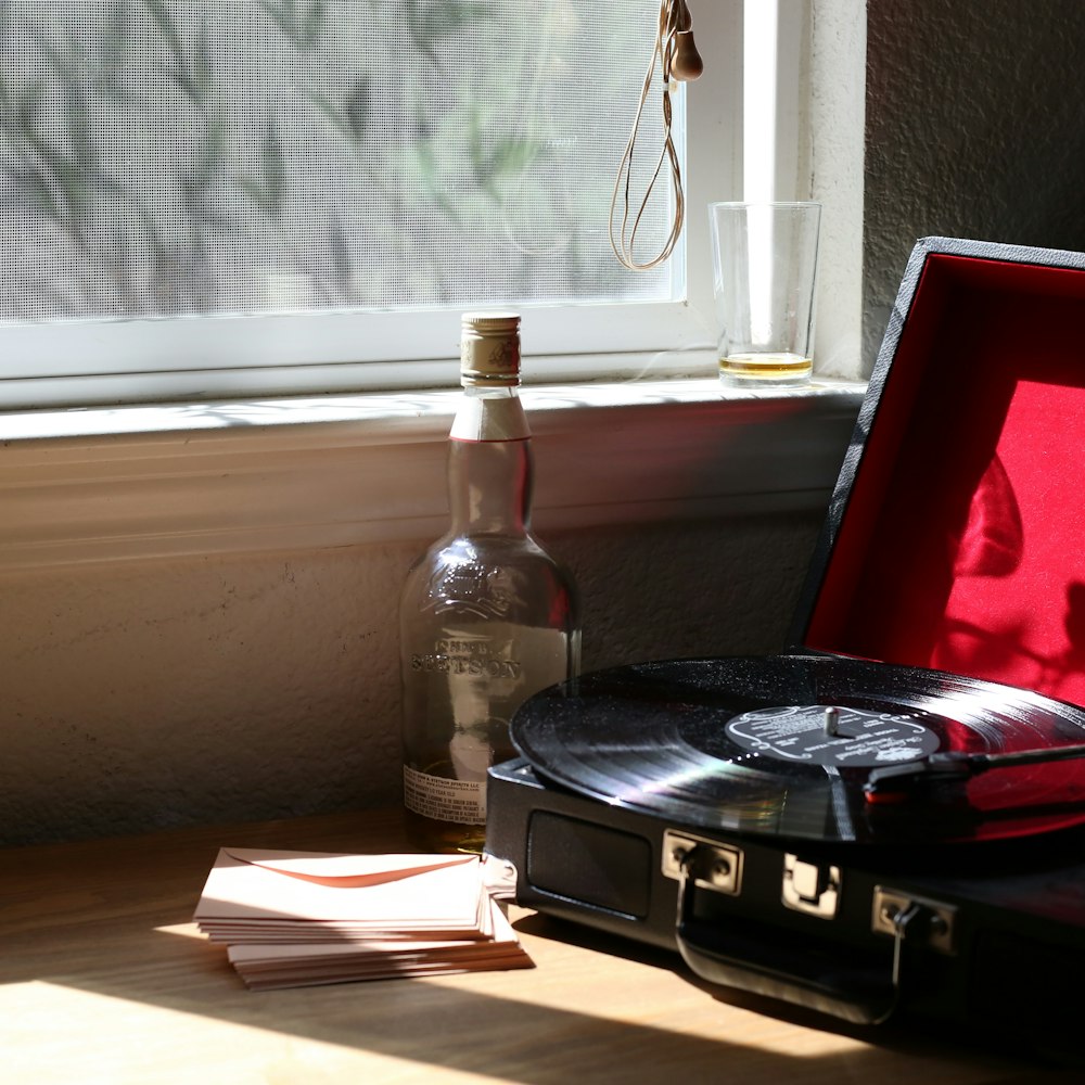 black and gray stereo turntable beside clear-glass bottle