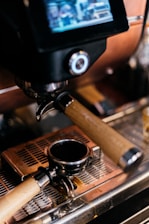 A close-up of an espresso machine focusing on the portafilter resting on a drip tray. The machine has a digital display above the group head.