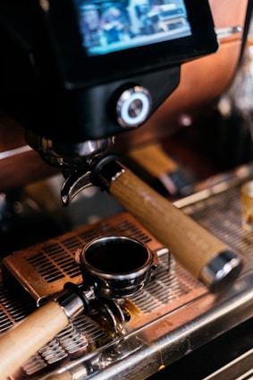 A close-up of an espresso machine focusing on the portafilter resting on a drip tray. The machine has a digital display above the group head.