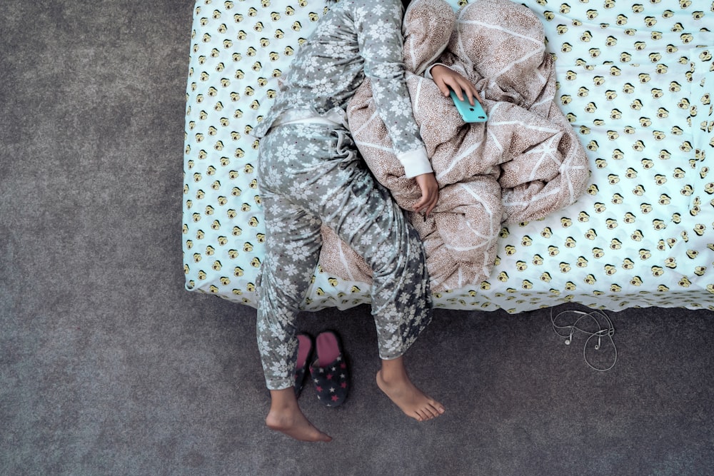 Kind im grau-weißen Pyjama liegt auf dem Bett und hält Telefon in der Hand