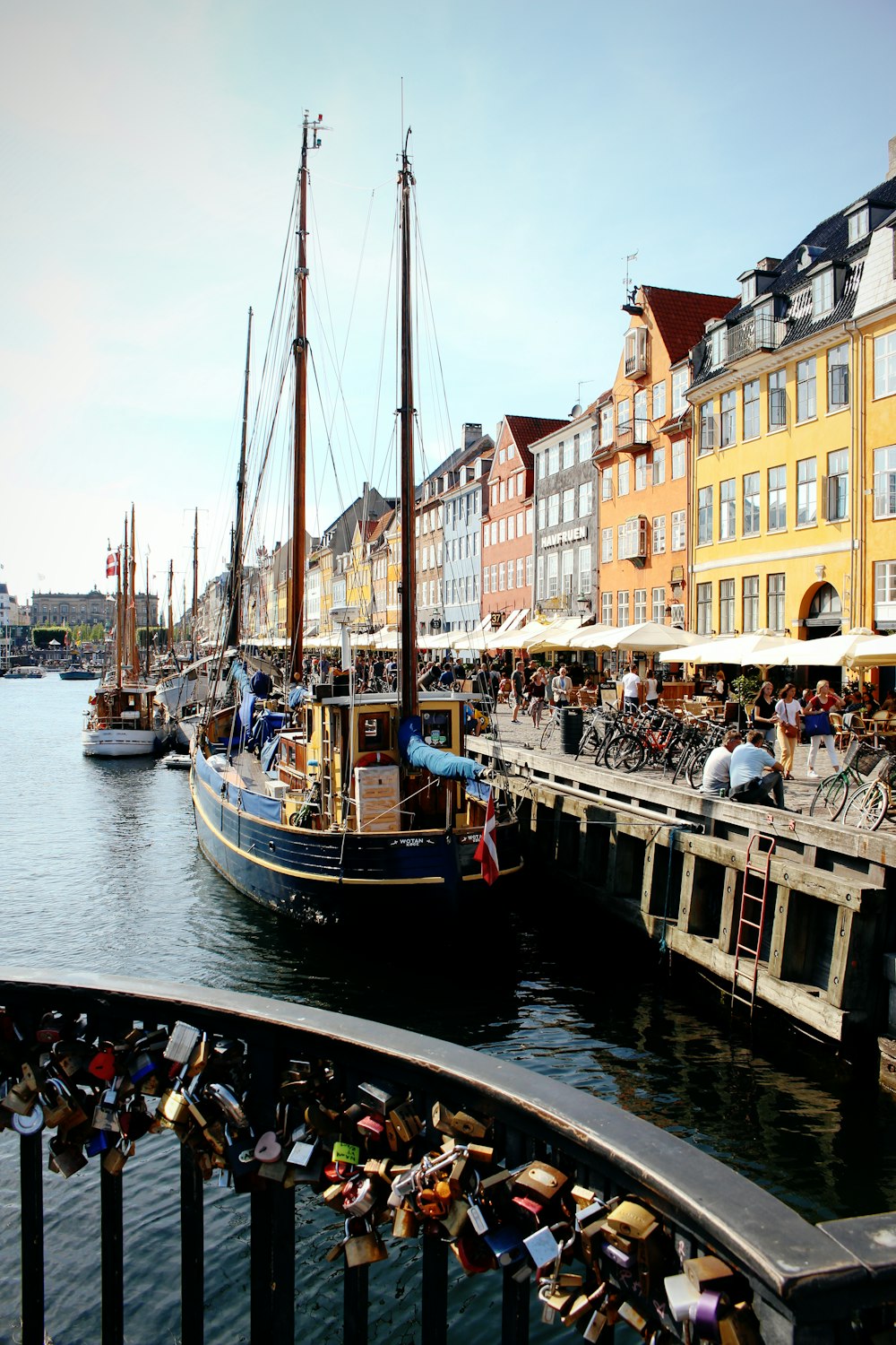 people near Nyhavn in Copenhagen buildings viewing boats on body of water under blue and white sky during daytime